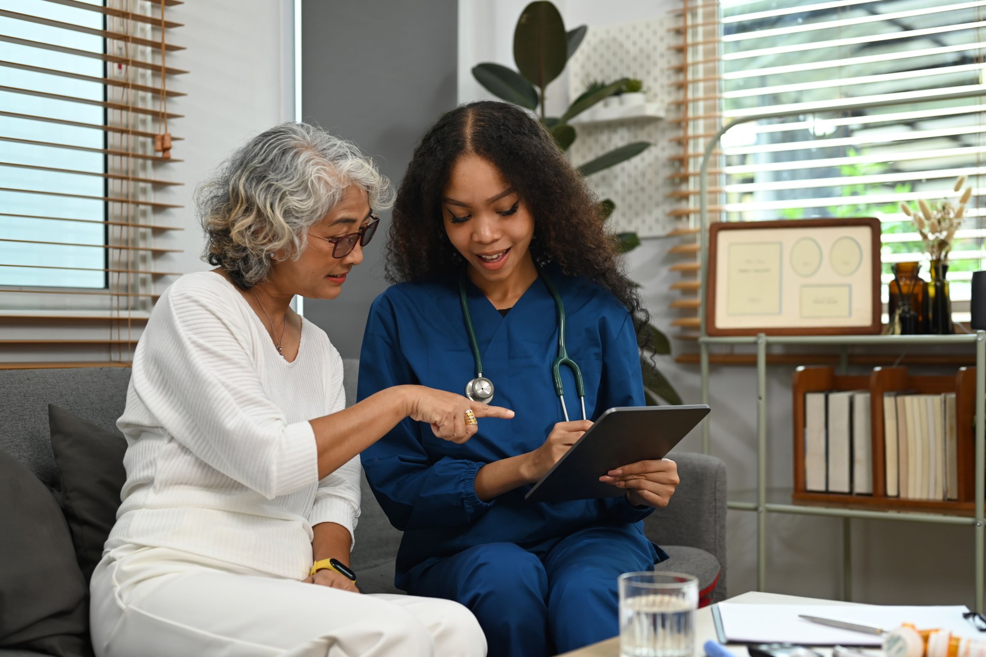 Practitioner nurse showing medical report to senior woman on digital tablet during home care visit. Elderly healthcare concept.